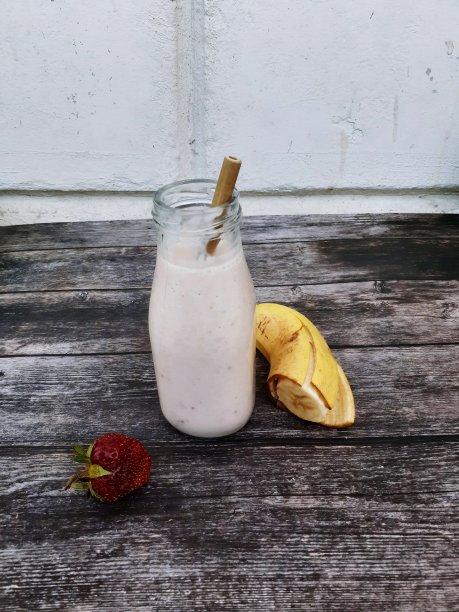香蕉和草莓冰沙在一个玻璃瓶子，竹吸管在深棕色的木头背景图片下载