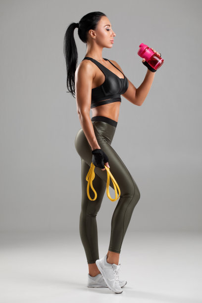 一个健康的女人从一个瓶子里喝水，孤立在灰色的背景。活泼的女孩止渴图片下载