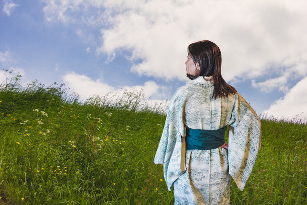 中年的日本模特正看着绿色的草地，草地上开着简单的花，从后面看。图片下载
