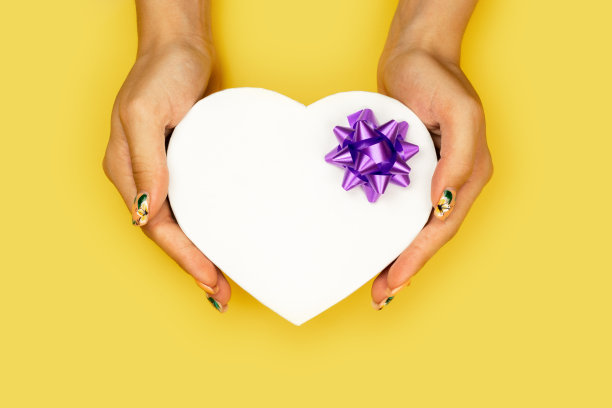 白色心形礼盒在女人的手孤立在黄色背景与复制空间。图片下载
