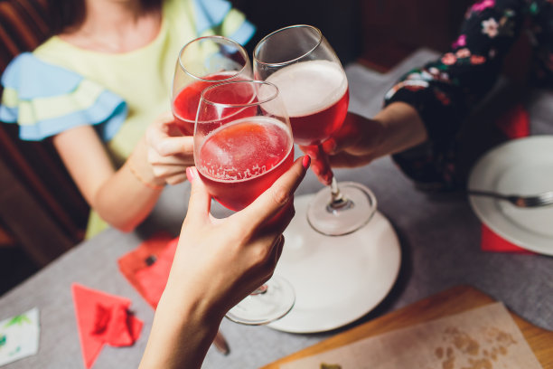 裁剪近距离照片的玻璃杯与香槟。年轻人正在举杯庆祝这一事件。桌子上摆满了美味的食物和饮料。图片下载