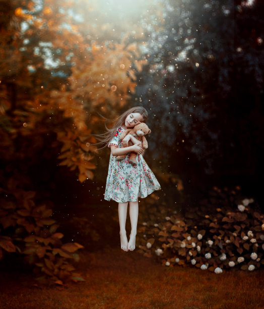 梦想着可爱的女孩，头发飞扬，手里拿着泰迪熊在地面上盘旋。孩子穿着轻薄的花图案长裙，在梦里和拥抱玩具，创意神奇的照片在空中图片下载