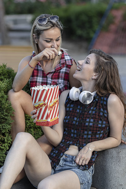 两个迷人的年轻长头发女人正在城市的街道上吃着爆米花玩图片下载