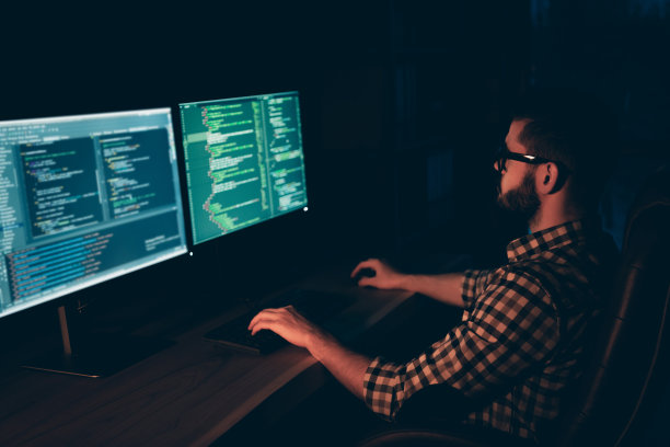 近距离的侧面资料照片帅气他他他的家伙程序员打字键盘开发外包IT处理语言两个显示器桌子办公室代理穿specs正装格子衬衫图片下载