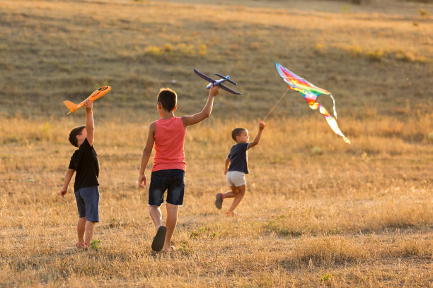 孩子们在操场上奔跑，三个男孩发射玩具飞机和风筝，在日落，在背光，概念，生活方式图片下载
