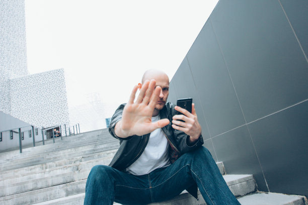 成人光头胡子严肃的男人坐在楼梯上用手关闭相机，没有更多的照片图片下载