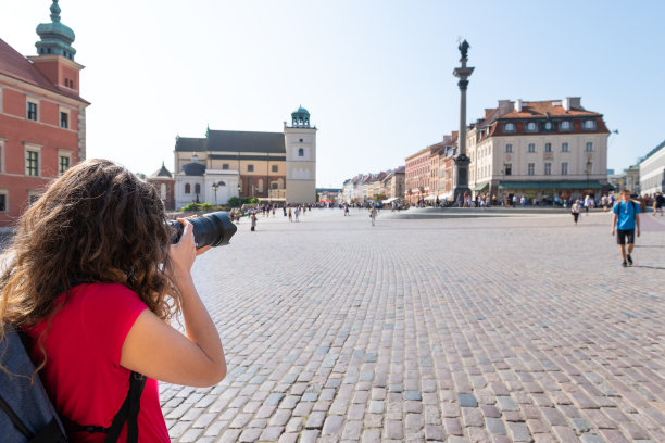 波兰华沙著名老城区历史悠久的城堡广场在首都城市建筑、城市景观天际线与纪念碑和女摄影师游客拍照留念图片下载