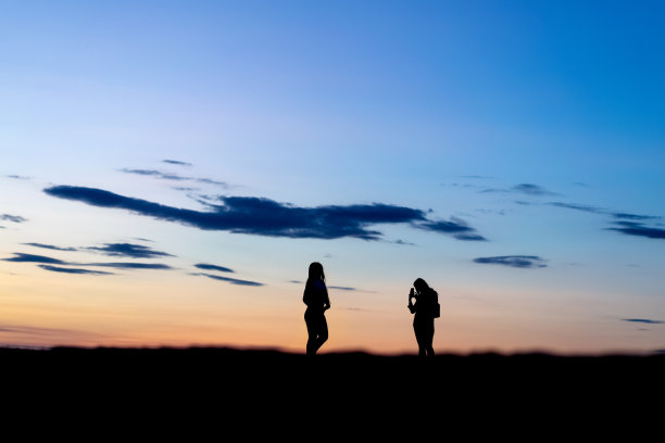 两个女人的剪影正在拍摄日落图片下载