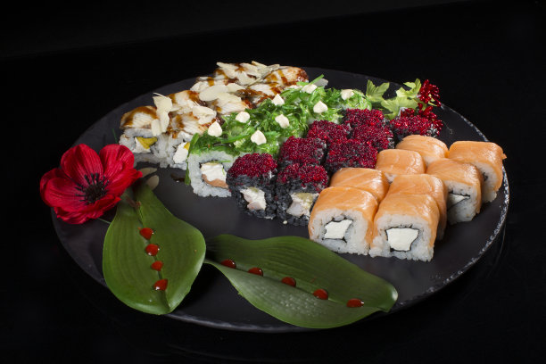 塞斯寿司的黑色背景。日本餐厅的菜单。几个寿司排列在盘子上，装饰着红莓、花和叶子图片下载
