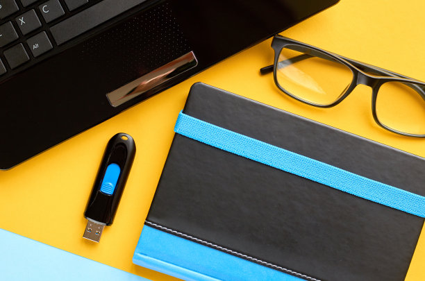 黑色眼镜，笔记本电脑，usb闪存和笔记本电脑键盘在蓝色和黄色的背景构成。图片下载