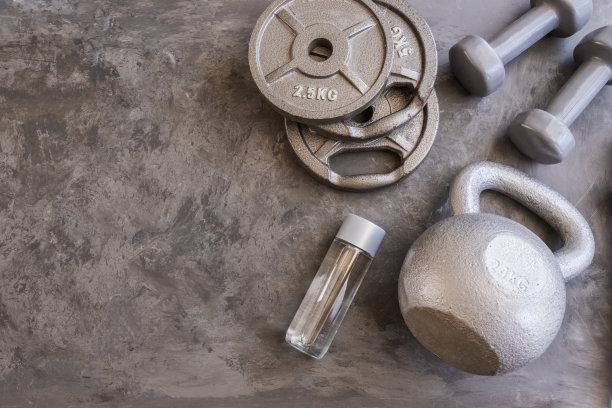 健身房水泥地板上的杠铃、灰色哑铃、壶铃和水瓶的重量板。重量训练和锻炼肌肉的设备。运动或锻炼的概念图片下载
