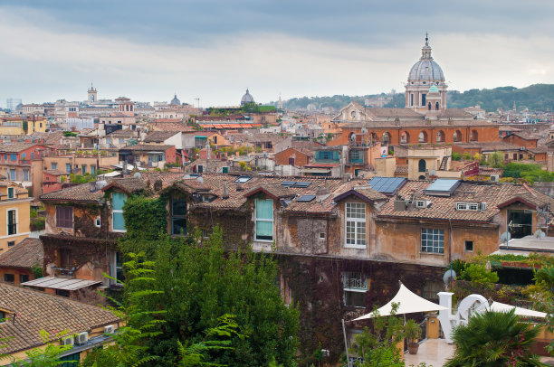 在许多古老的石头建筑的屋顶和穹顶之间有一个花园和花盆，桔子树和绿树和植物在戏剧性的多云的秋天天空下图片下载