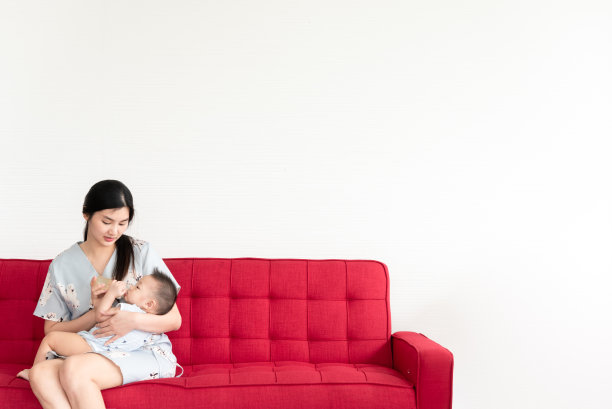 单身妈妈在红色沙发或沙发床上给她8个月大的宝宝喂奶图片下载
