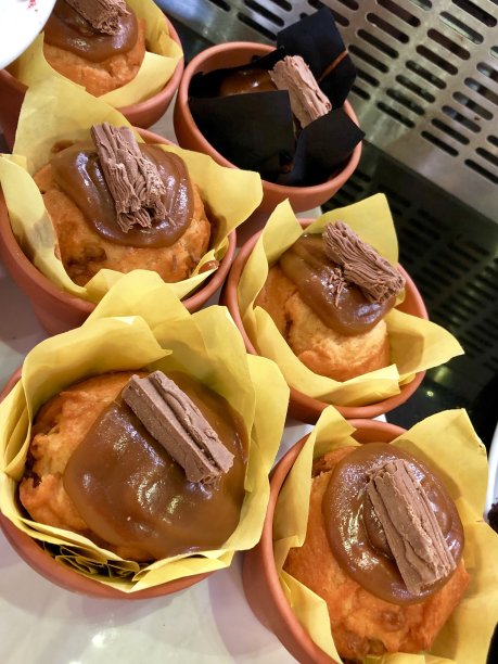 太妃焦糖松饼的图片展示在小赤陶土花盆和黄色烘焙纸上，放纵的蛋糕上面有太妃焦糖酱和一个薄片巧克力棒图片下载