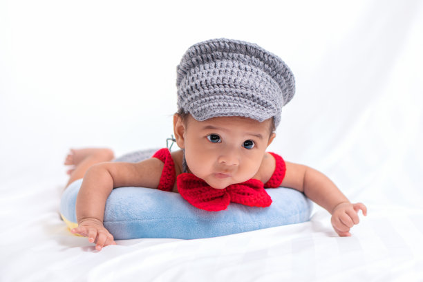 一幅亚洲婴儿的肖像，戴着灰色的帽子，躺在一个枕头上，背景是白布图片下载
