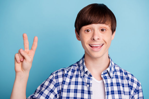 肖像迷人的青少年做v符号看起来穿着格子衬衫孤立在蓝色背景图片下载