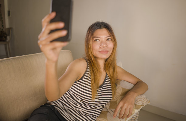 年轻迷人的生活方式肖像和放松的30多岁亚洲印尼女人躺在家里客厅沙发上的手机舒适的自拍照片使用在社交媒体上图片下载