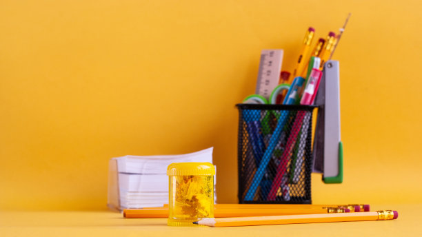 明亮的现代极简主义文具用于学校作业，放在一个用作办公用品的玻璃里，旁边是一张便签纸，一个黄色的卷笔刀，黄色的背景上有黄色的铅笔。回到学校的概念。图片下载