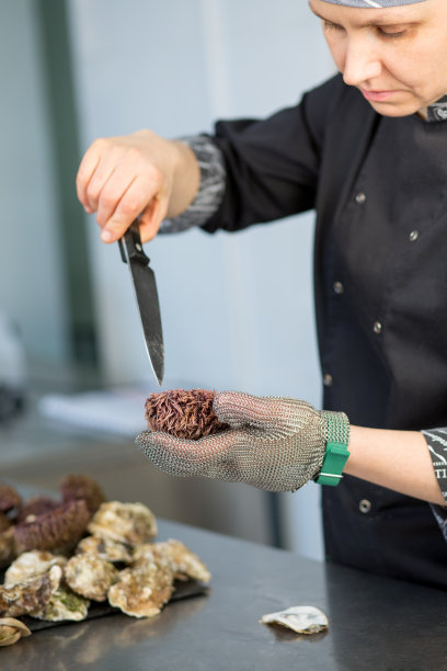 厨师站在一家餐厅的厨房里切海胆。一个手与一把刀在金属手套的特写图片下载