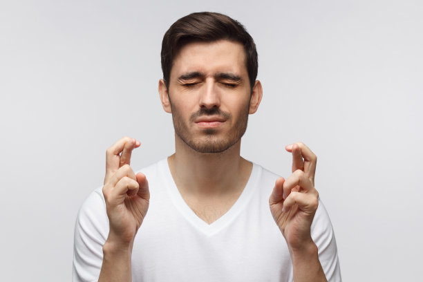 年轻人紧闭双眼，双手交叉，目光深沉，祈求好运，祈祷，孤立在灰色的背景上图片下载