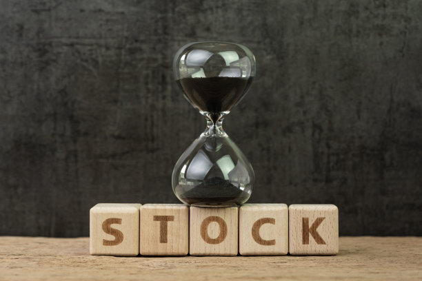 股票市场倒计时，金融危机或长期投资，沙漏或沙漏在木方块上，在木桌上用字母建筑单词stock，黑色背景图片下载