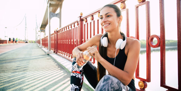 近距离的照片可爱的微笑运动和苗条的女人是坐在水和耳机后跑步和休息图片下载