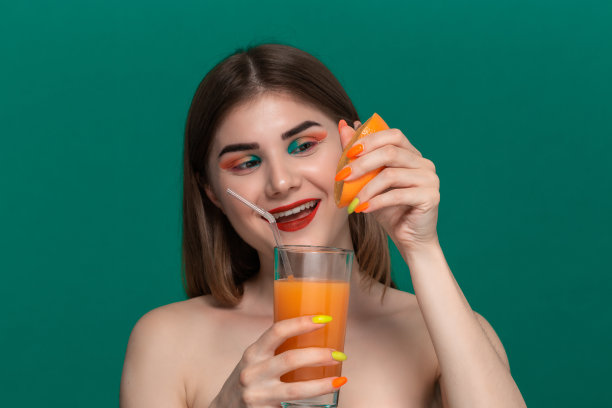 特写美丽的年轻女子与明亮的颜色化妆挤橙汁出一个橙色的一半图片下载
