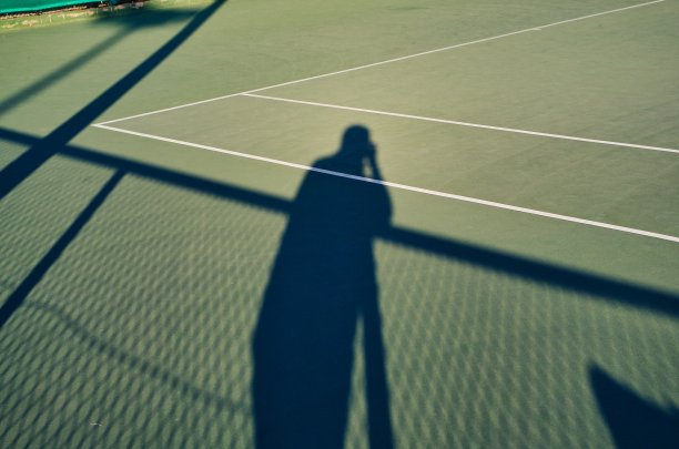 一个运动摄影师的影子在网球场上形成对比图片下载