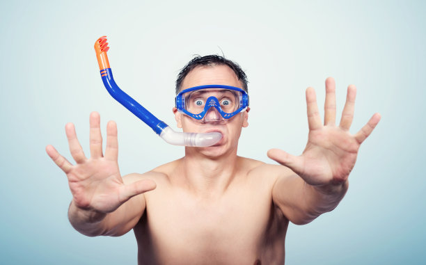 年轻男子戴着潜水镜在孤立的蓝色背景下，双手张开做着停止标志，表情严肃的恐惧，防御手势图片下载