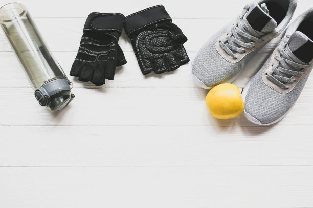 运动的照片。健康的生活方式。装水的瓶子，苹果和皮手套。时尚运动鞋。白色木制背景。完美的平面。图片下载