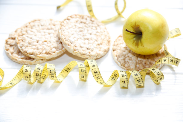 运动的照片。健康的生活方式。健康的概念。低脂脆面包和水果。适合身体的卷尺。白色木制背景。完美的平面。图片下载
