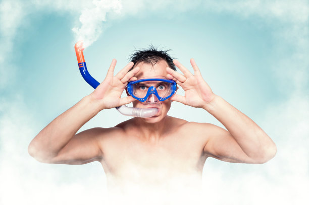 年轻男子戴着游泳面罩，嘴里含着通气管，嘴里冒出白烟。全浸的概念。图片下载
