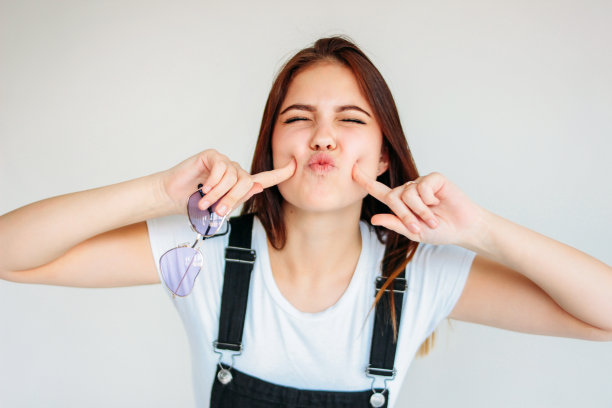 快乐无忧无虑有趣的十几岁的女孩与黑色的长发在心形太阳镜和白色的t恤孤立图片下载