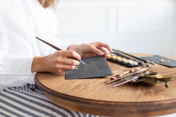 一位书法家拿着一支有墨水的笔，用手写字体在一张卡片上签名。特写镜头。软的焦点。图片下载