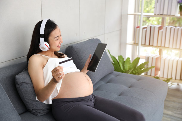 年轻孕妇持平板电脑听音乐，用信用卡进行网上购物图片下载