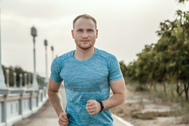 一个穿着蓝色t恤和黑色短裤的白人男子在日落时在柏油路上训练和奔跑的肖像图片下载