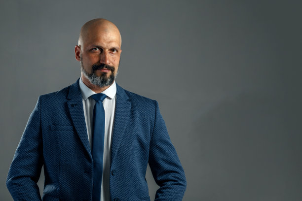 残忍的秃顶、留着胡子的商人，穿着一套经典的西装，背景是灰色的，有复印空间图片下载