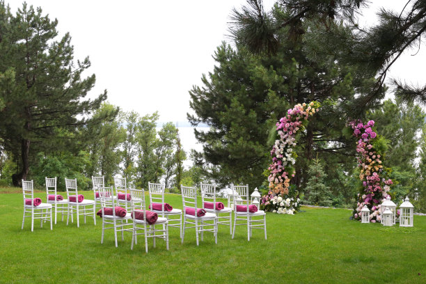 白色木制空椅子排成一排，绿色草地上有花卉拱门。婚礼装饰。图片下载