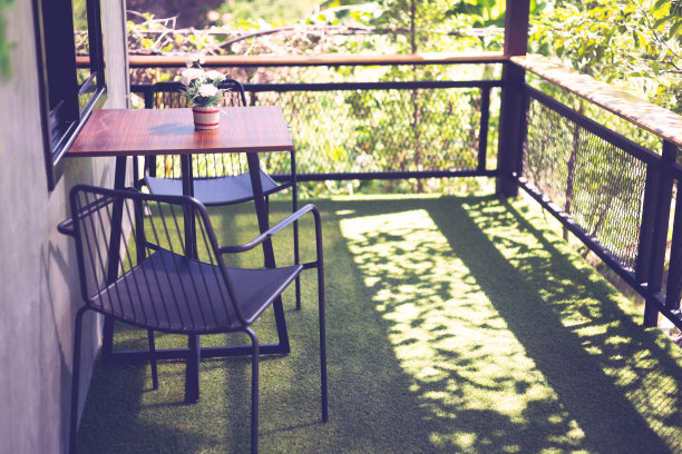 墙边摆放着桌子和钢制椅子，绿色塑料草坪在复古的阳光下图片下载