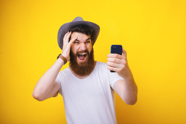 一张帅气的大胡子男子的照片，拿着手机，看着屏幕，黄色的背景图片下载