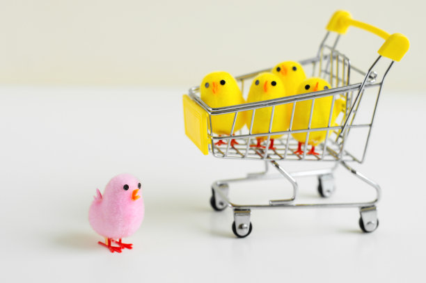 一个粉色的小鸡玩具站在白色的背景和四个小的小鸡玩具在购物车里。领导的概念图片下载