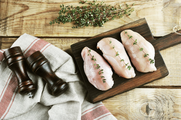 生鸡胸放在木板上。该组合辅以绿色百里香和一块布餐巾。以复古风格处理照片。从以上观点。图片下载