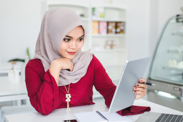 年轻的亚洲穆斯林妇女在白咖啡店里用平板电脑。图片下载