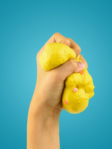 孩子的左手捏着蓝色背景上的黄色黏液。图片下载