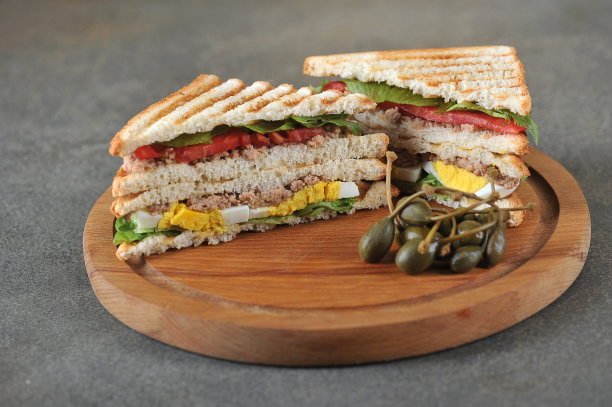 两份金枪鱼三明治。三明治旁边的一个圆形木托盘上放着酸豆。图片下载