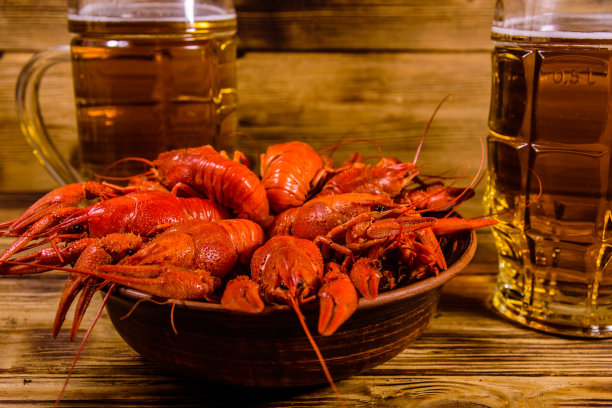 木桌上放着两杯啤酒和煮小龙虾图片下载