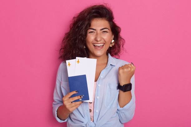 照片中的女学生手里拿着护照和登机牌机票，像胜利者一样握紧拳头，感到高兴，买了机票，想去国外旅行，在粉红色的背景上孤立。图片下载