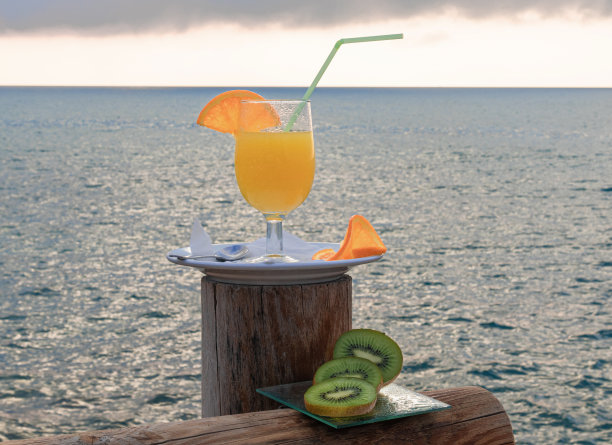 美味的彩色照片绿猕猴桃片，橙片，一杯橙汁和大海的背景图片下载