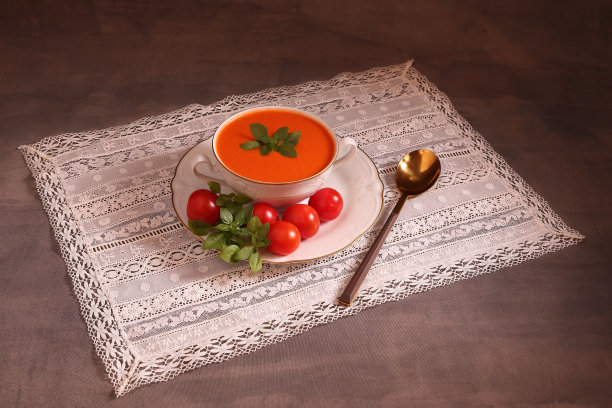 番茄凉菜汤配青椒、罗勒、洋葱、黄瓜和橄榄油，放在白色杯子里，配有金色勺子和白色绣花桌布图片下载