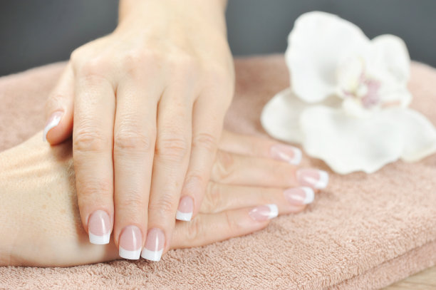 法国修指甲。画面中，两个女人的手搁在一条毛巾上。靠近那朵白色的兰花。图片下载